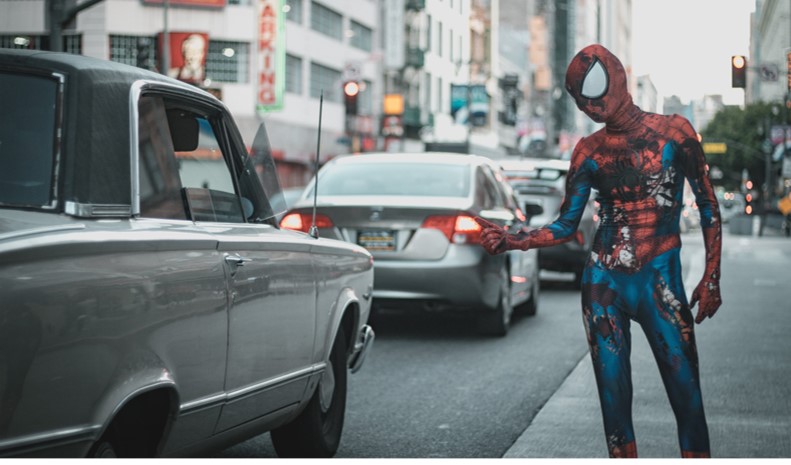 Spiderman standing in a street talking to someone in a car